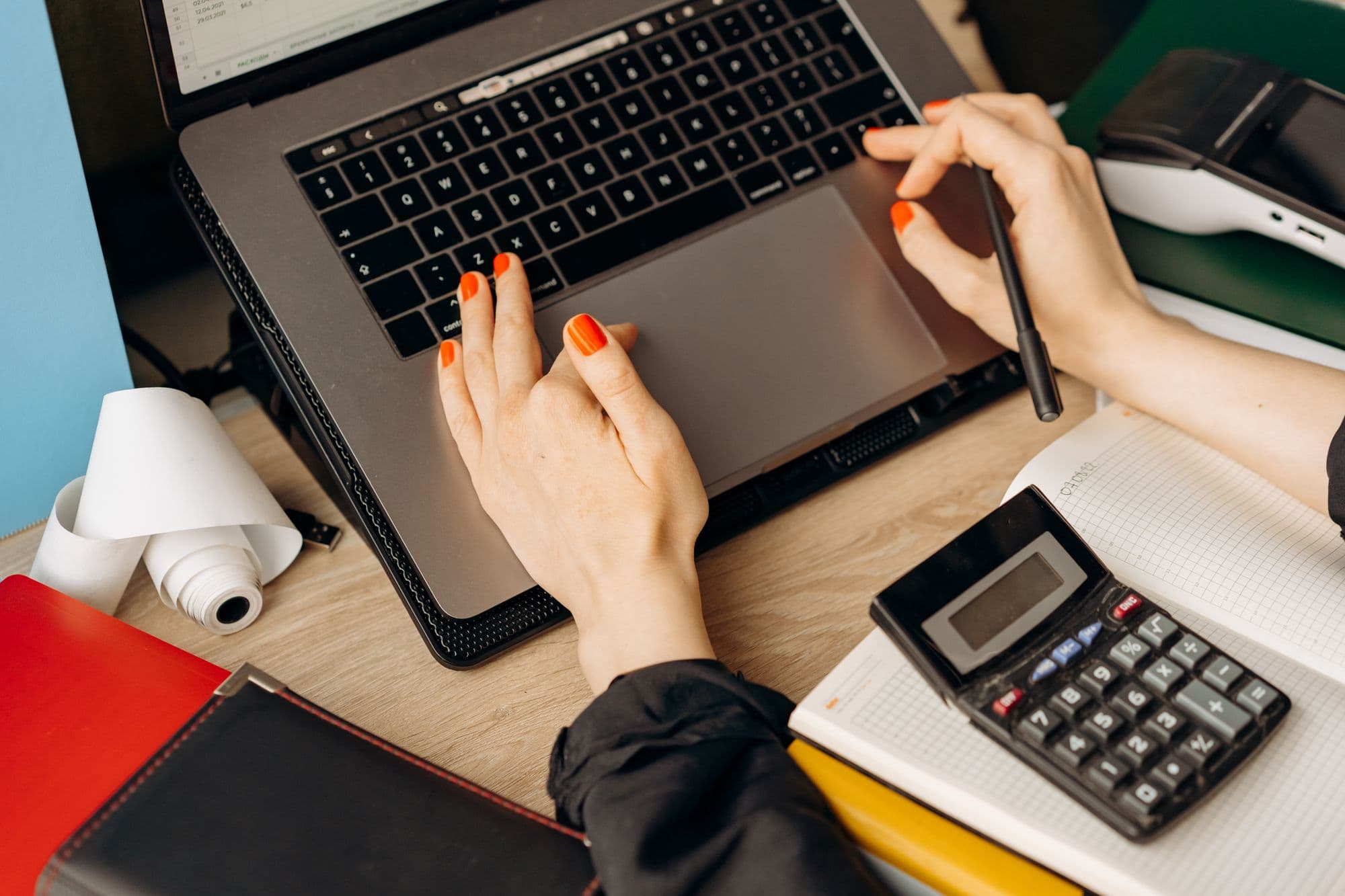 Hands working on a laptop beside a calculator and printed statements
