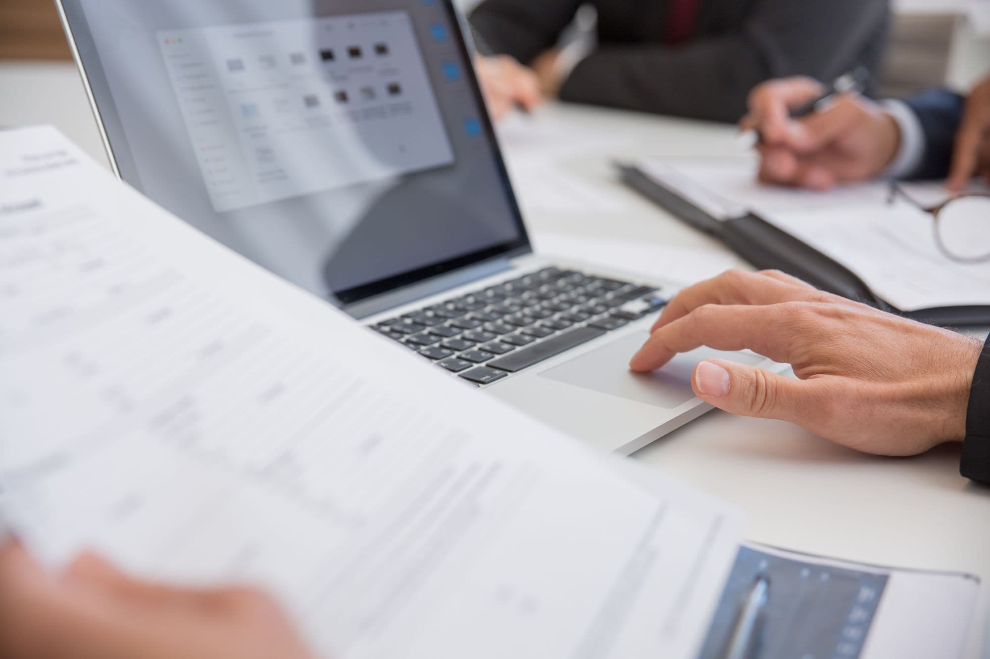 Hands typing on a laptop beside printed documents